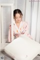 A woman in a pink robe sitting on a white bed.