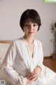 A woman sitting on top of a bed in a white shirt.