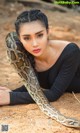 A woman laying on the ground with a snake around her neck.