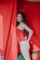 A woman in a red bodysuit posing in front of a red curtain.