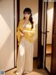 A woman in a yellow kimono standing in front of a door.