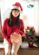 A woman in a red sweater and a santa hat holding a present.