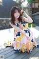 A woman in a colorful dress sitting on a wooden deck.